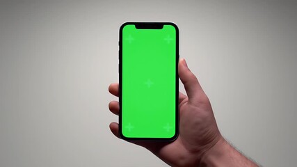 Hand holding modern smartphone with green screen for mockup display against a neutral background.