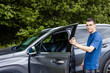© Natalia - Young guy in glasses opens the door of his car, smiles, watches camera