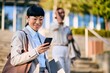 © bnenin - Asian Businesswoman Using Smartphone Outside Modern Office Building on Sunny Day