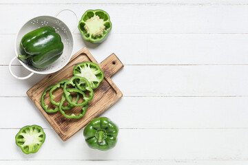 Wall Mural - cutting board and colander with green bell peppers on white wooden background