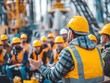 © GoshaMovies - A safety supervisor in a hard hat conducts a briefing for a team of workers at a construction or drilling site. This represents leadership, instruction, and workplace safety meetings.