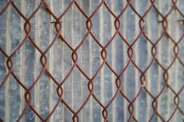 A close-up perspective of a rusted wire fence against a textured background presents industrial textures and geometric patterns. Rust colored metal links creates visual interest.