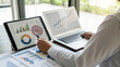 ©  Blar Studio - Professional analyzes financial data on laptop and tablet, charts and graphs for strategic planning in a modern, bright office space for success