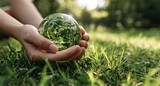 Hands hold a crystal globe of greenery, representing Earth, on grass