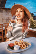 © EdNurg - Young woman wearing a hat enjoying a glass of white wine and a plate of fried calamari with french fries in an outdoor restaurant