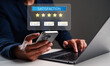 © Rawat - A person checking satisfaction ratings on a smartphone while using a laptop, highlighting digital feedback and reviews.