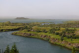 Scenic view of small islands and lava formations surrounded by blue waters of Lake Mývatn in Iceland. The green vegetation softens the rugged volcanic rock, creating a balance between raw geology and 