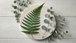 © Creative_johirul - Fern leaf and eucalyptus on a wooden board with a white background