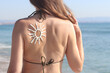 © Mariia - Sun image made with sunscreen on woman's back. Sunbathing on the beach. Close-up. Woman in swimsuit on the beach, back view. Using sunscreen. Concept of beach vacation, seaside resort, beach holiday
