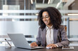 © Tetiana - Successful and smiling young African American woman working in the office at a laptop, holding an online meeting