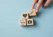© Thecreator T - Hand placing wooden block with syringe icon on top of health related icons on a light blue surface
