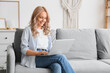 © Pixel-Shot - Beautiful blonde woman using laptop on sofa at home
