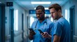 © Ediane - Two medical professionals in scrubs are intently looking at their smartphones in a brightly lit hospital hallway, deep in concentration.