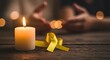 © Edina - A lit candle and a yellow ribbon on a wooden surface with blurred hands in the background creating September 10th, World Suicide Prevention Day