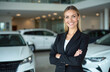 © Viktor - Pro woman in black suit smiles with crossed arms in auto dealership showroom. Cars in background. Automotive business, sales career opportunity, client trust and vehicle presentation concept.