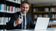 © Curioso.Photography - A confident, smiling man with glasses gives a thumbs up while sitting at a laptop, representing approval, productivity, online work, or digital communication.