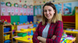 © Curioso.Photography - A smiling woman, likely a preschool or elementary school teacher, stands confidently with her arms crossed in a colorful classroom filled with toys and learning materials.
