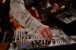 © TrueFrame Collective - Caucasian man adjusting modular synthesizer while playing electric guitar, focusing on hand turning knob with visible instrument cables and blurred background