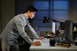 © Stella 16 - A man is stand at a desk at night with a computer and a keyboard. He is looking at the computer screen