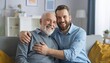 © SSuperTier - A heartwarming scene of an adult hipster son with a beard hugging his elderly father at home.,