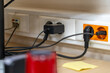 © sommersby - Row of power outlets and data ports with plugs and cables, including black charger and orange outlet, illustrating busy connection hub in modern office or home setting.
