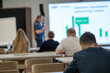 © Anton Gvozdikov - Blurred conference audience watching speaker presenting on a screen with displayed graphs.