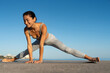 © sutulastock - Smiling woman practicing side lunge yoga stretch outdoors under a clear blue sky