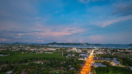 Wall Mural - Aerial hyper lapse view of A breathtaking sunset paints the sky in vivid hues of orange and blue over a coastal town, with lush green hills framing the scene. cloud in dramatic sunset over the ocean