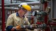 © Viktor_D - Factory worker in PPE checking gauges, steel pipelines and valves in background.