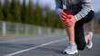 © Maksym - Athletic woman outdoors on running track, bent over holding her knee with clear red pain marker, health awareness concept of chronic injury and rehabilitation