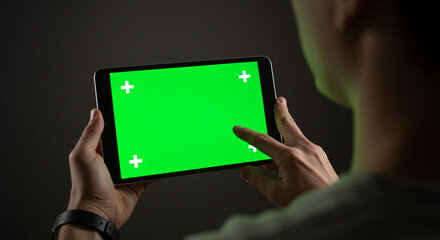 Person's hands holding and touching a tablet with a green screen display, ready for content creation