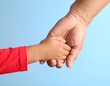 © gelas - Two hands clasped together, a child's and an adult's, against a light blue background.  A child in a red shirt