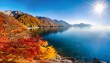 © Judith - a serene autumn day by the sea with golden and red leaves on the mountainsides the calm water reflecting the vibrant colors and the sun shining brightly