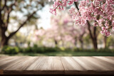 Wooden table in foreground with blurred pink cherry blossoms and trees in background wood surface