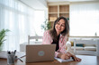 © Migma_Agency - Happy woman working from home taking notes watching laptop