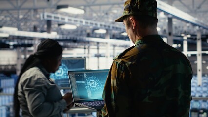 Soldier in engineering role uses AI application on laptop to manage server hub systems. Army commander reviews secret intelligence information using artificial intelligence in data center, camera B