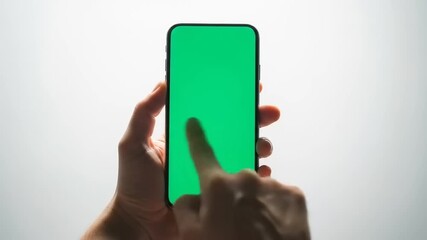 Person's hands holding a smartphone with a green screen, finger touching the display, on a white background.