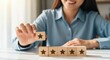 © David Zarzosa - Smiling woman holding star rating wooden block for customer satisfaction, positive feedback and five stars quality evaluation.