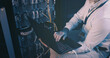 © peopleimages.com - Cables, coding and hands with laptop, server room and network engineering with tech and electrician. Data center, technician and person with app for software upgrade, troubleshooting and online