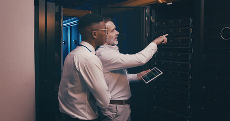 Men, tablet and team in server room with inspection, point and talk with mentor for system upgrade. People, tech and assessment with app, software update or programming for cybersecurity solution