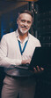 © peopleimages.com - Laptop, portrait and database with man in server room for data center, network or systems. Cybersecurity, software technician and cloud computing with mature person for hardware maintenance and code