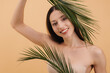 © anatoliycherkas - Beautiful smiling woman holding palm leaves is posing on beige background