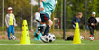 © matimix - School boy dribbling soccer ball in slalom training drill. Football training camp for school kids. Soccer practice equipment on grass pitch