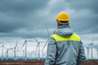 © Tohamina - Worker in safety gear overlooking a wind farm under a cloudy sky