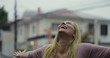 © Marco - Blonde woman smiling joyfully in residential street under rain, looking up with emotional release and happiness, immersed in moment of personal joy