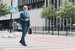 © deagreez - Confident businessman in formal suit walking through urban crosswalk with briefcase and coffee on a sunny day