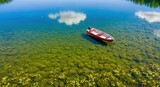 Solitary red boat on clear reflective lake with lush underwater vegetation