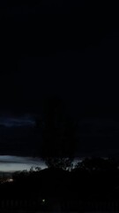 Wall Mural - A stunning time lapse captures the sun setting behind a mountain silhouette, with a beautiful orange and red light painting the evening sky and clouds