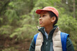 © Seventyfour - Black boy wearing cap and backpack standing in forest looking to side, appearing thoughtful, outdoor setting suggesting exploration or hiking, child age group evident