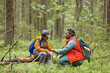 © Seventyfour - Black woman supporting Black girl while sitting together in forest, both wearing backpacks, woman holding girl's hand, showing care and encouragement during outdoor activity